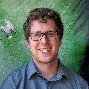 A man wearing glasses and a grey shirt is smiling for the camera.