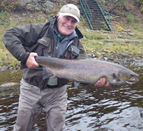 A man is holding a large fish in front of a river