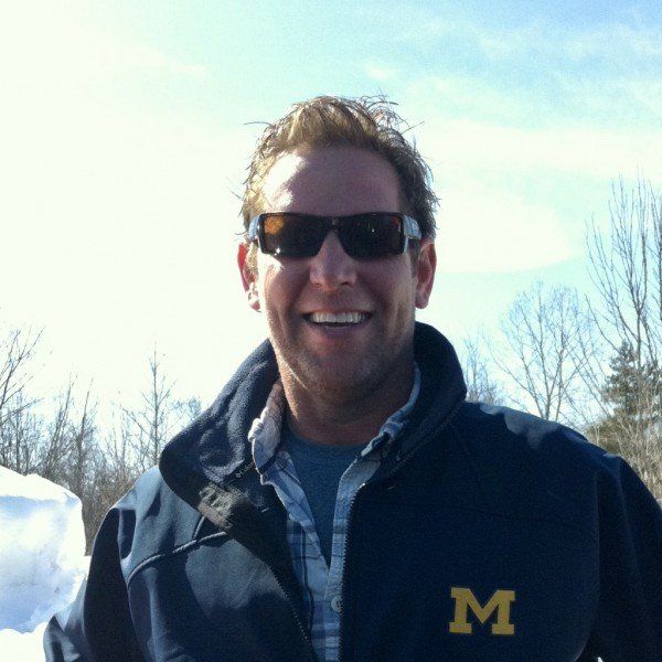 A man wearing sunglasses and a jacket with the letter m on it