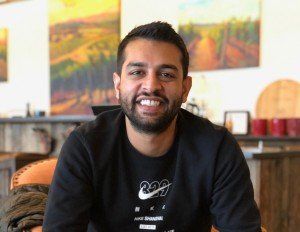A man with a beard is wearing a black nike shirt and smiling.