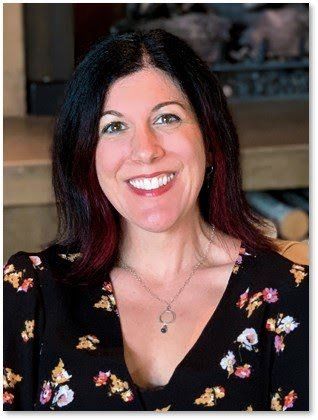 A woman wearing a floral shirt and a necklace is smiling for the camera.