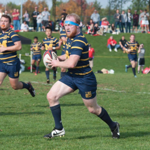 A man in a blue and yellow striped shirt is running with a rugby ball