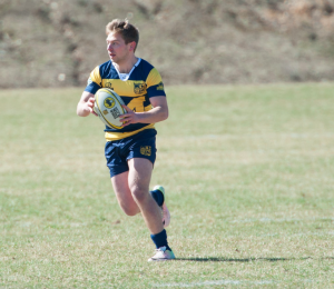 A man is running with a rugby ball on a field