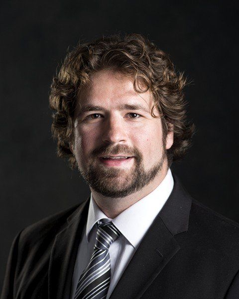 A man with curly hair and a beard is wearing a suit and tie.