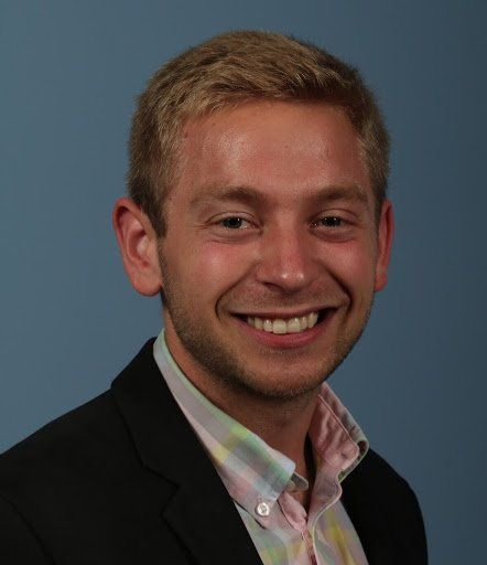 A man in a suit and pink shirt is smiling for the camera.