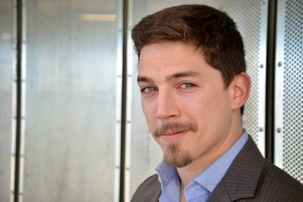 A man with a beard is wearing a suit and a blue shirt.
