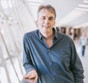 A man in a blue shirt is standing next to a railing in a hallway.