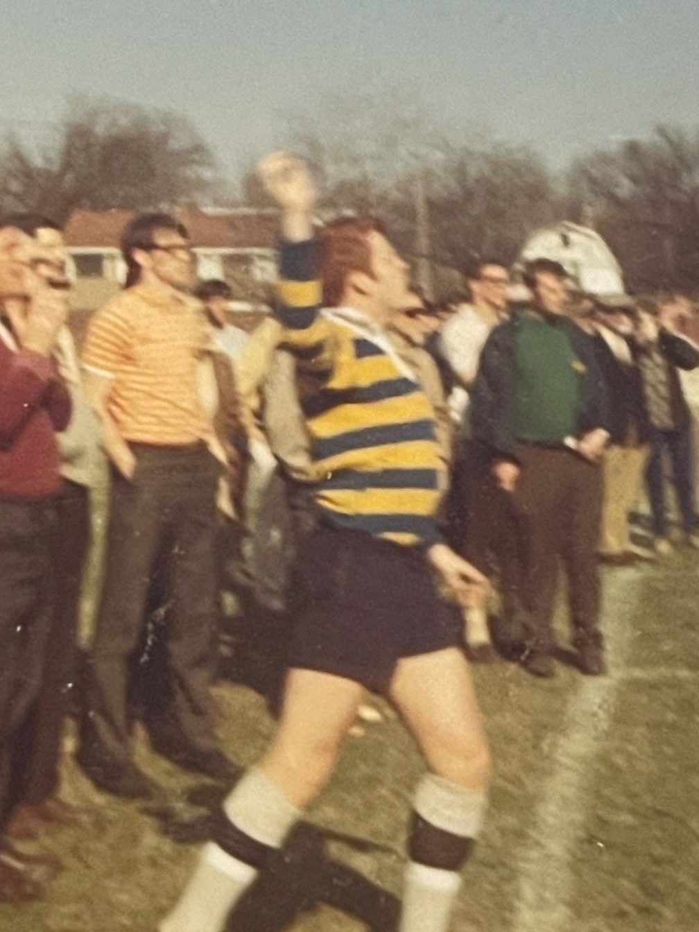 A man in a yellow and blue striped shirt is jumping in the air