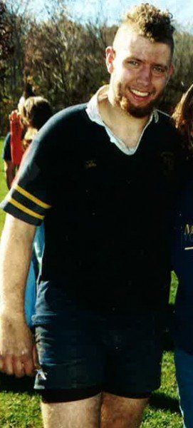 A man in a black shirt and shorts is smiling for the camera.