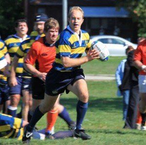 A man in a blue and yellow striped shirt is holding a rugby ball