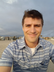 A man in a striped shirt is taking a selfie on the beach.