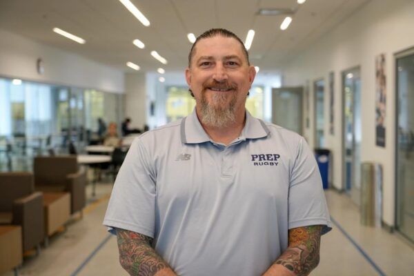 A man wearing a blue shirt with the word prep on it is standing in a hallway.