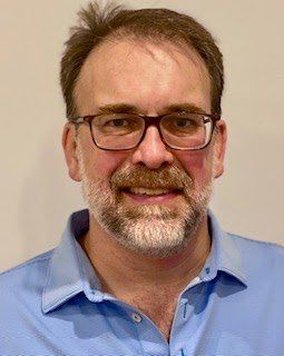 A man with a beard and glasses is wearing a blue shirt.