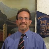 A man wearing glasses and a tie is standing in front of a painting.