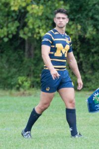 A man in a striped shirt with the letter m on it is walking on a field.