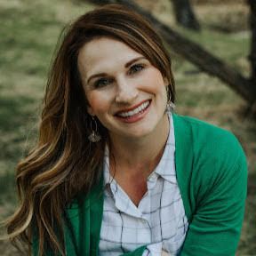 A woman wearing a green cardigan and a plaid shirt is smiling for the camera.