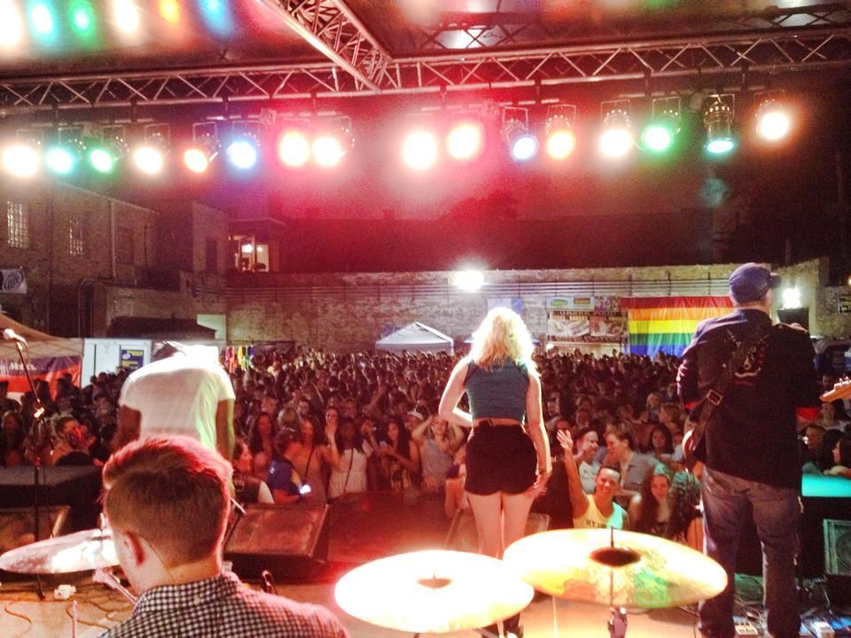 A group of people standing on a stage with a rainbow flag in the background