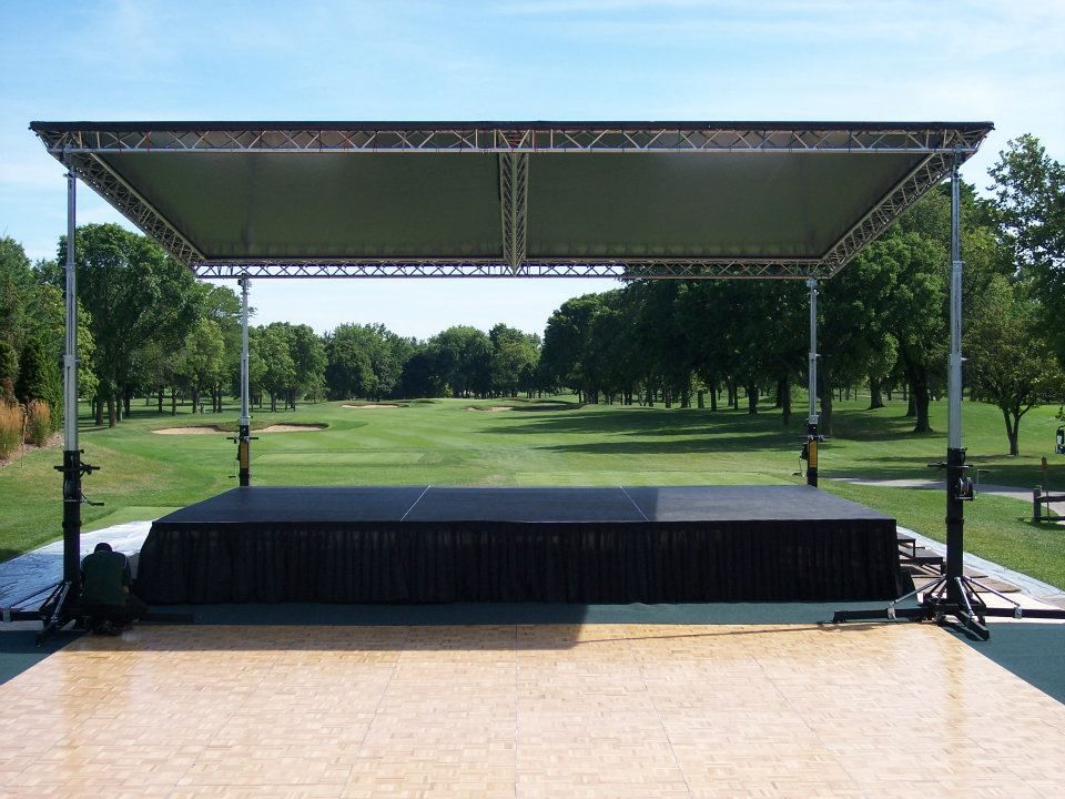 A stage with a canopy over it is sitting in front of a golf course.