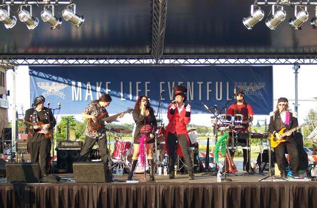 A band is performing on a stage under a banner that says make life eventful