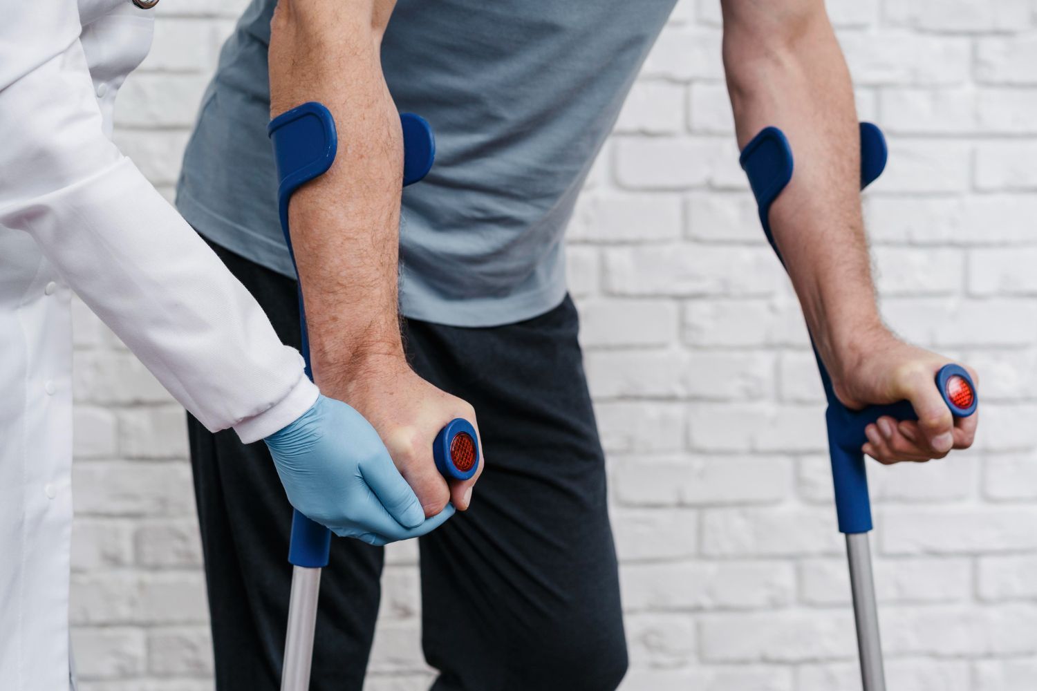Person using crutches, with blue wrist and arm support bands, in a clinical setting