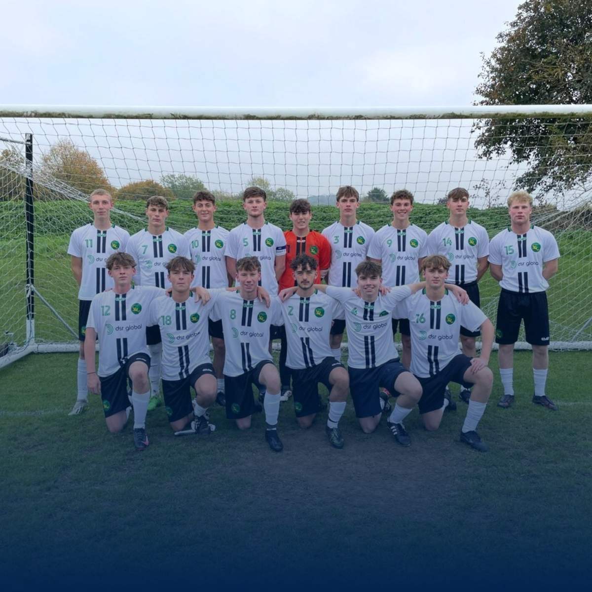 Soccer team posing in front of a goal; wearing black and white jerseys.