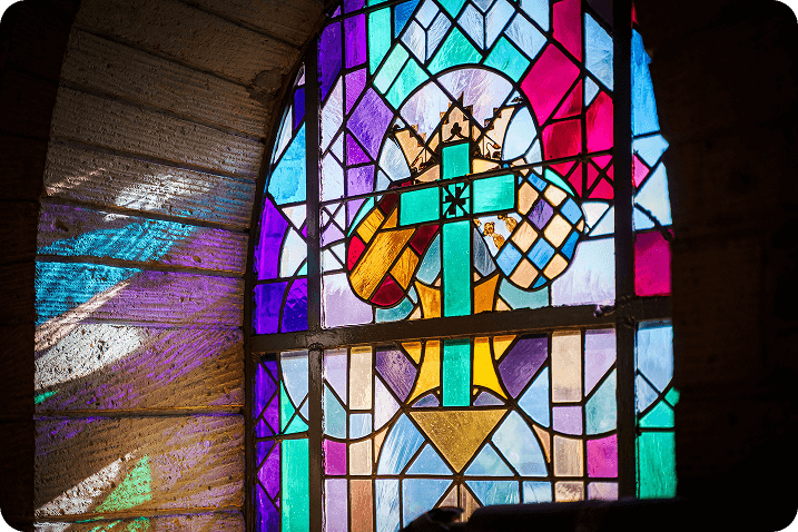 Stained glass window with a cross in a stone wall, casting colorful light.
