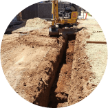 A yellow excavator is digging a trench in the dirt.
