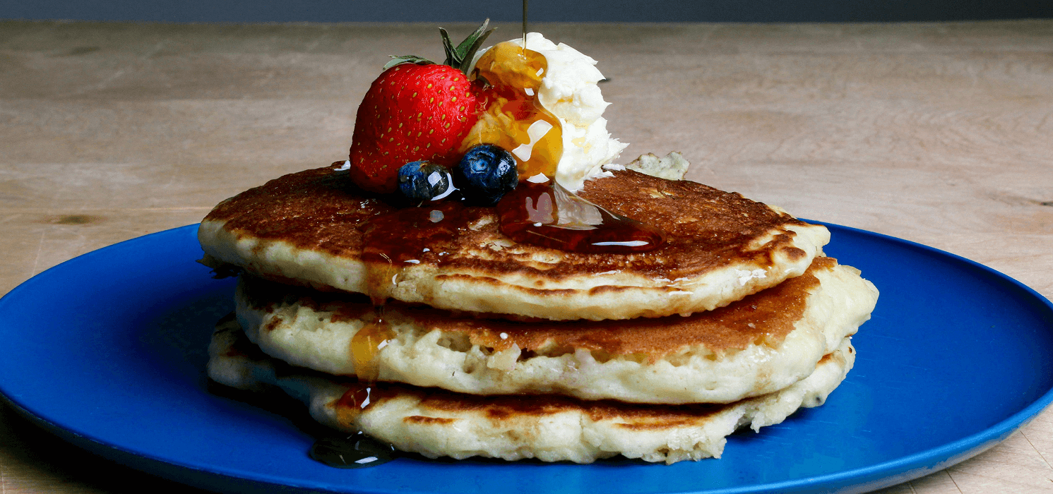 A stack of pancakes with syrup and berries on a blue plate.
