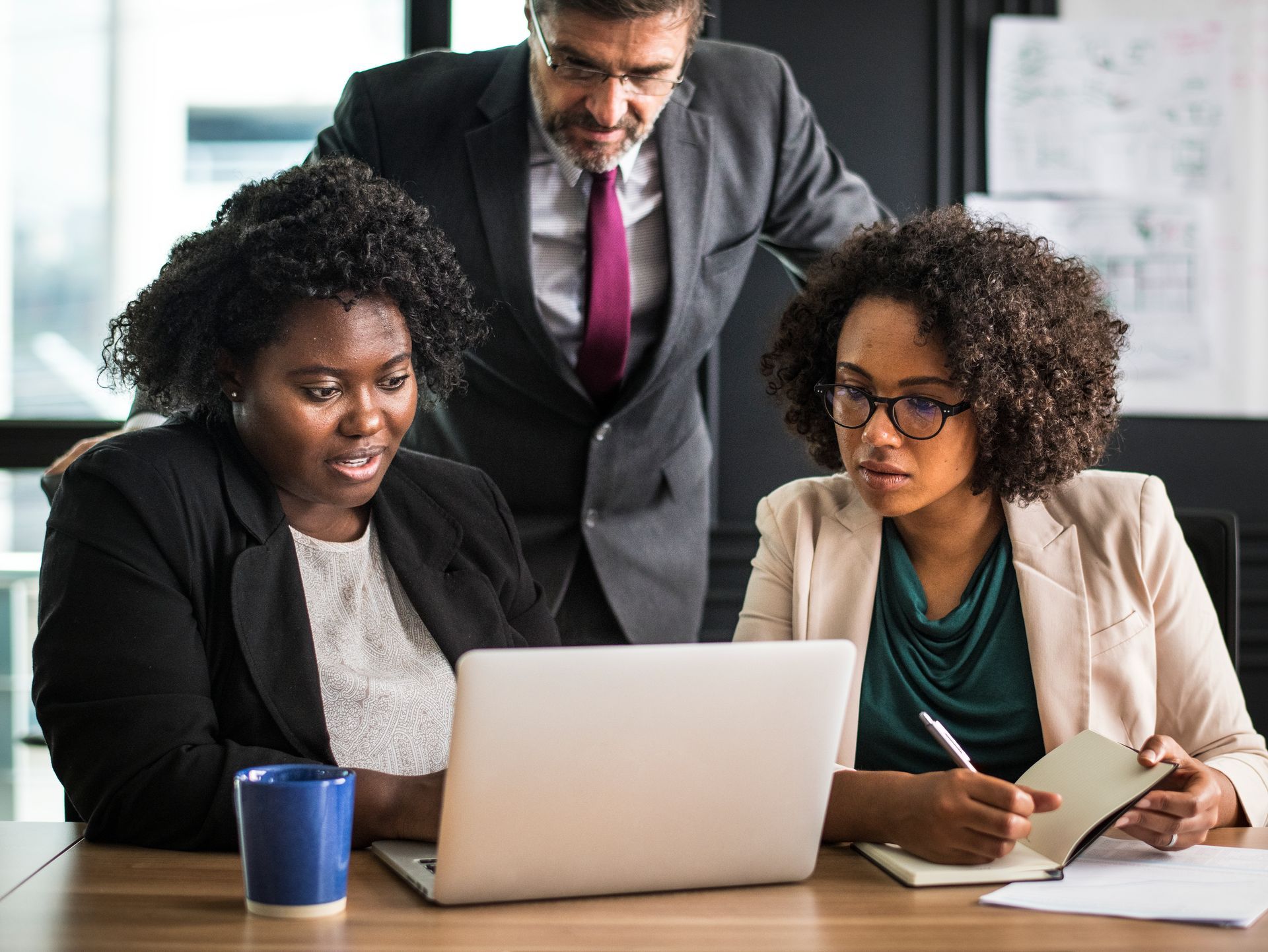 Three people in business attire looking at a laptop in an office.
