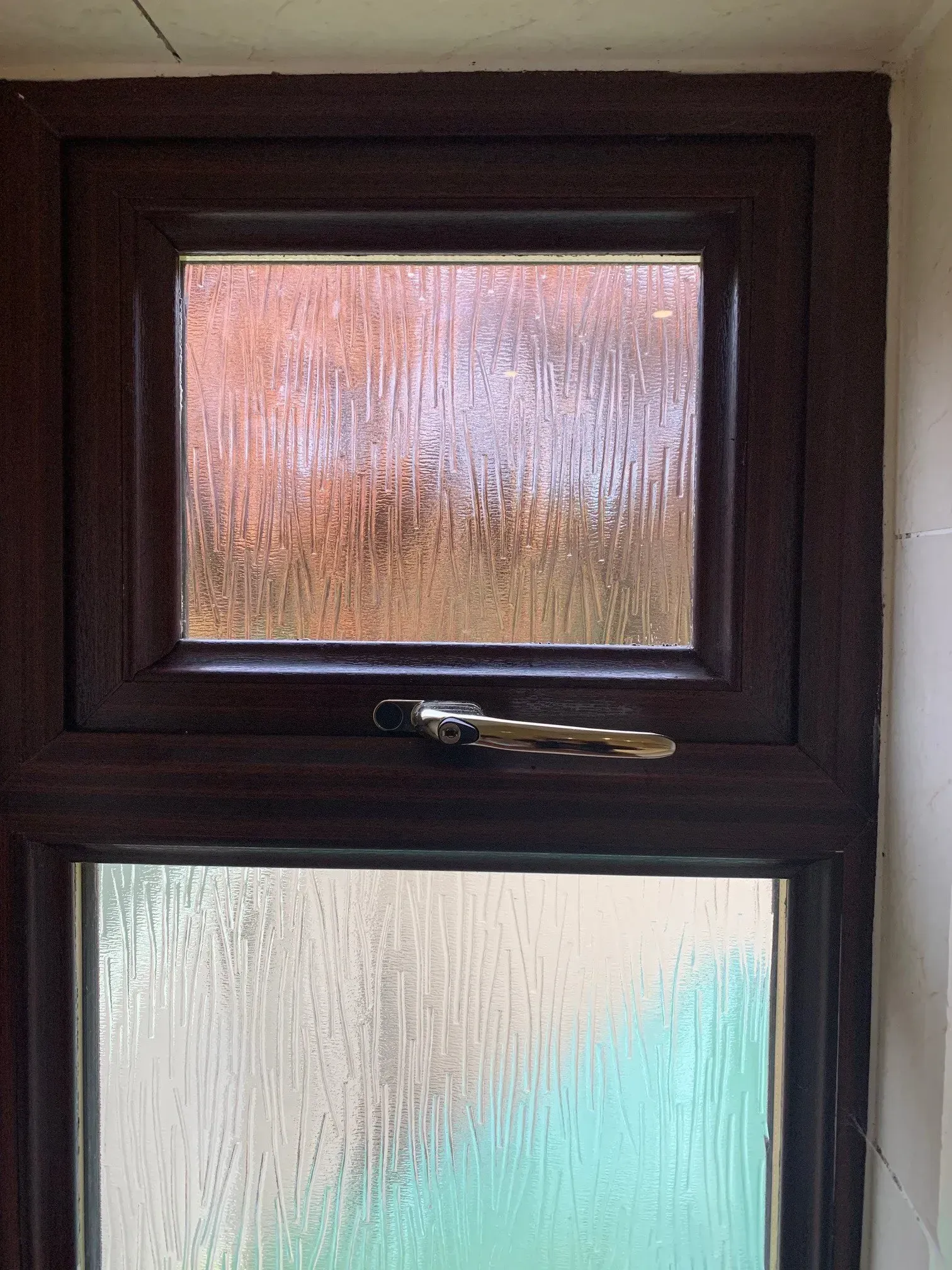 Brown framed window with textured glass, handle in the middle.