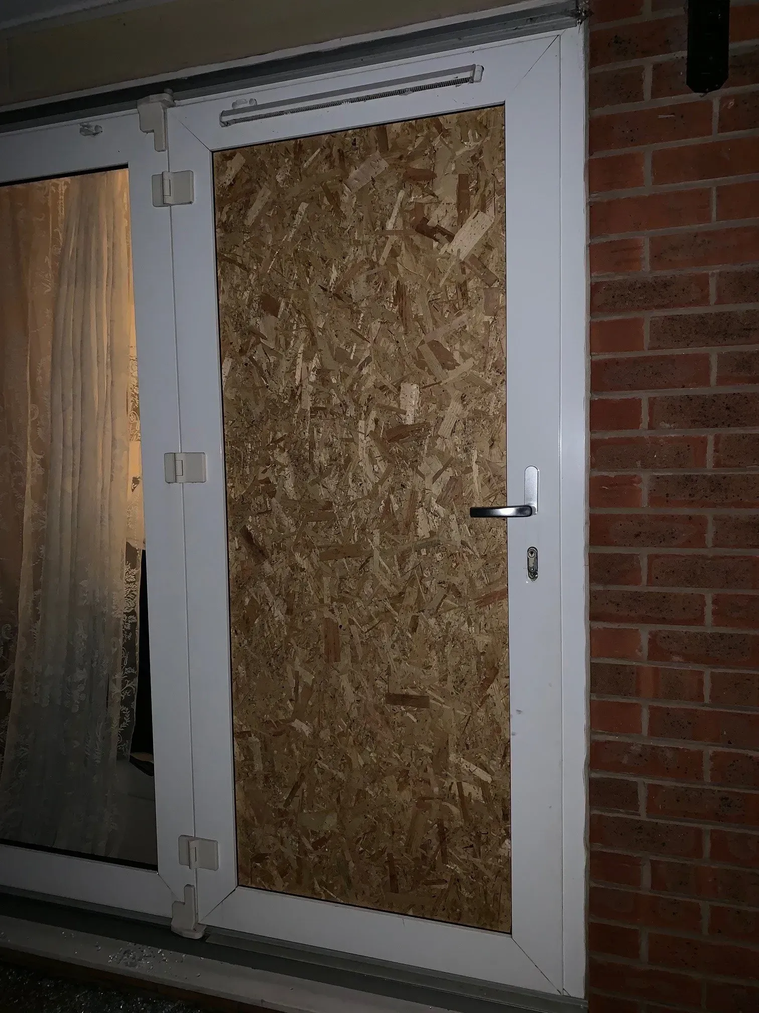 White-framed door covered with plywood. Brick wall to the right, glass door panel on the left.
