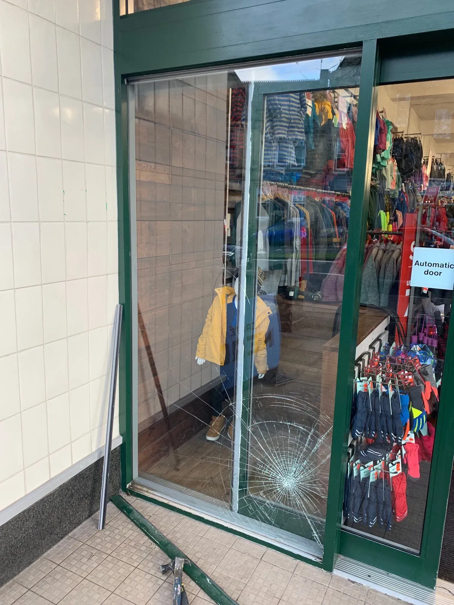Broken glass door at a retail store entrance; interior visible with clothing racks.