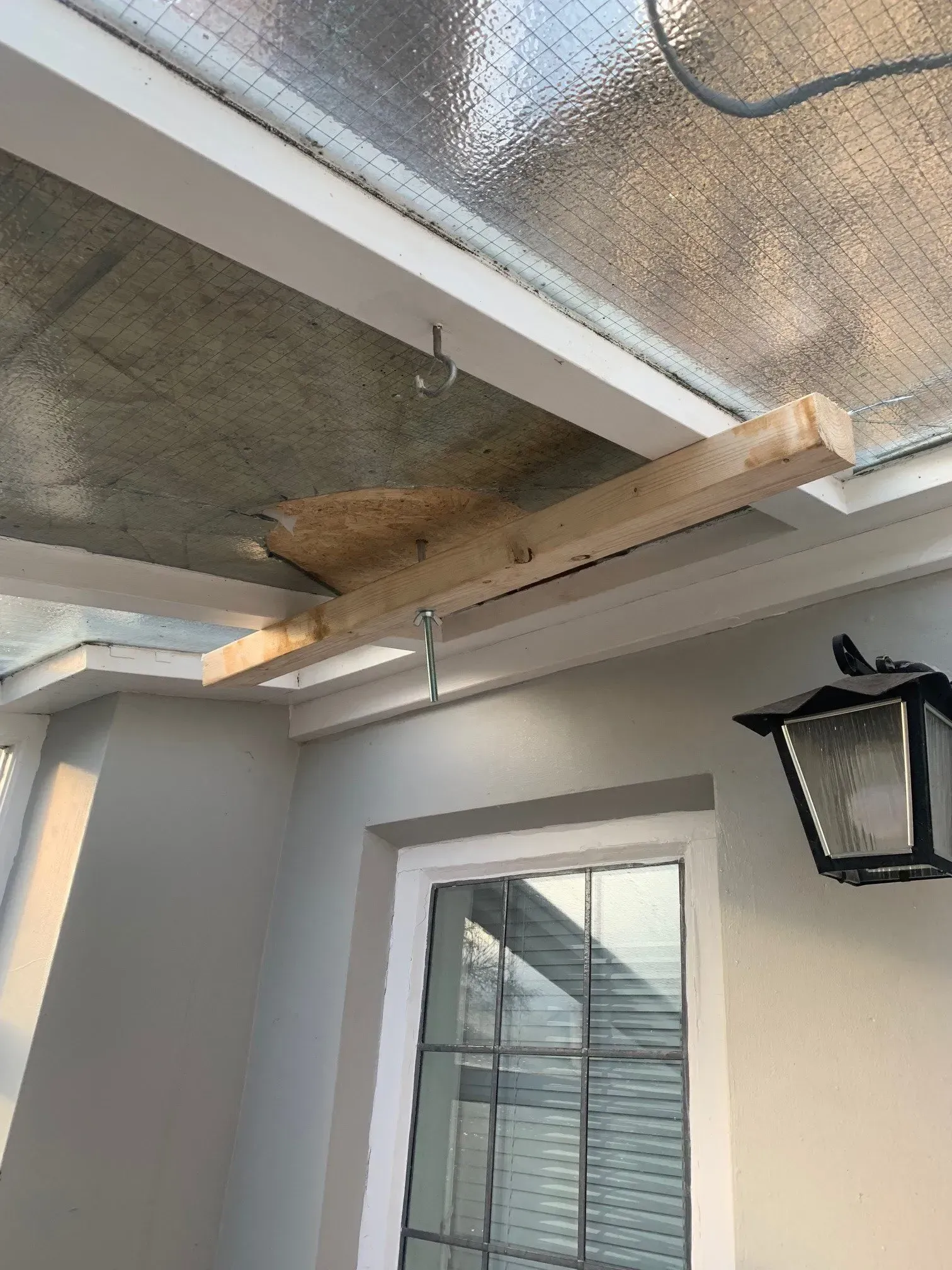 Wooden beam temporarily supporting a ceiling section in a room with a window and outdoor lamp.