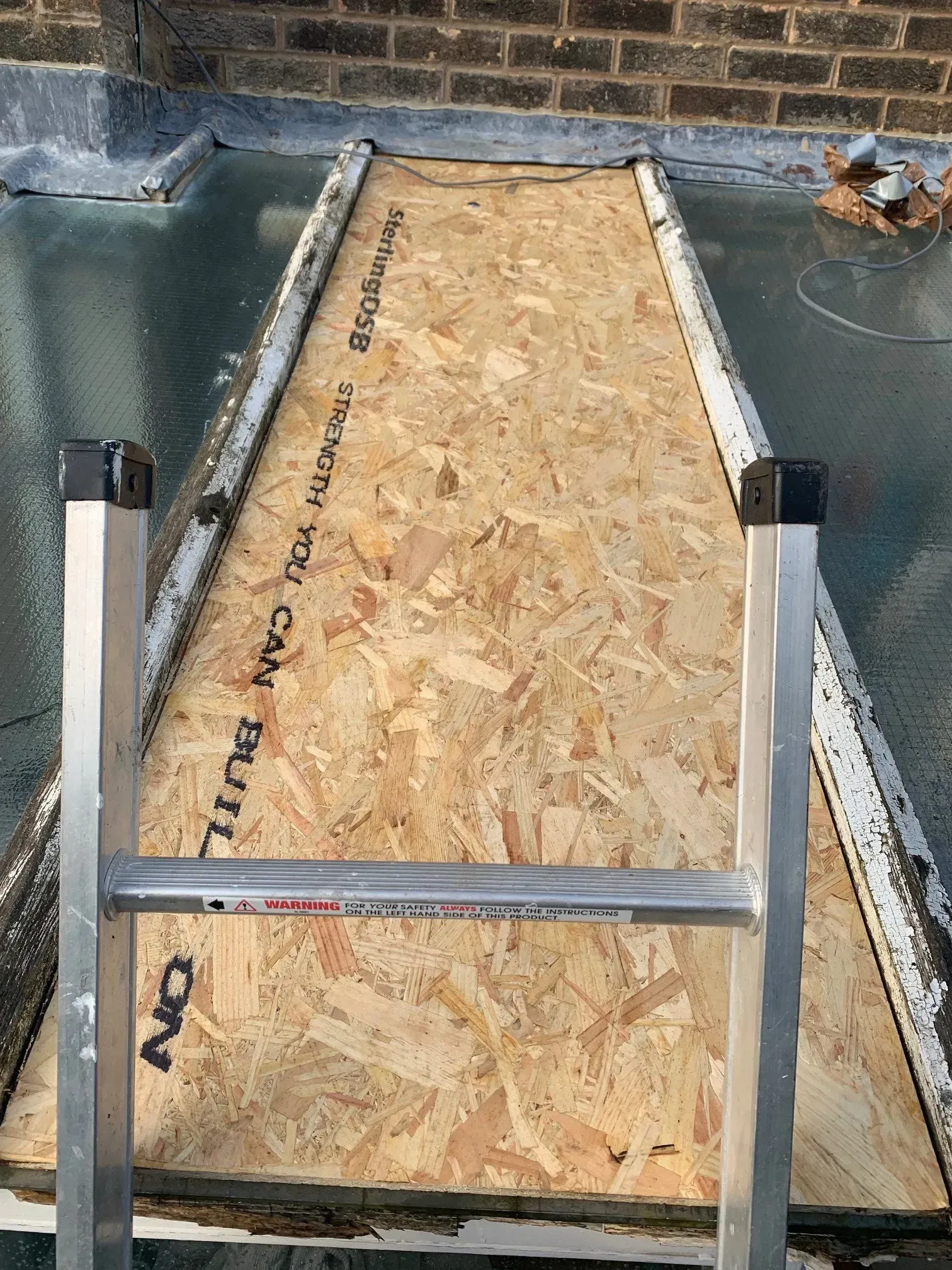 Ladder on a flat roof with OSB board pathway.