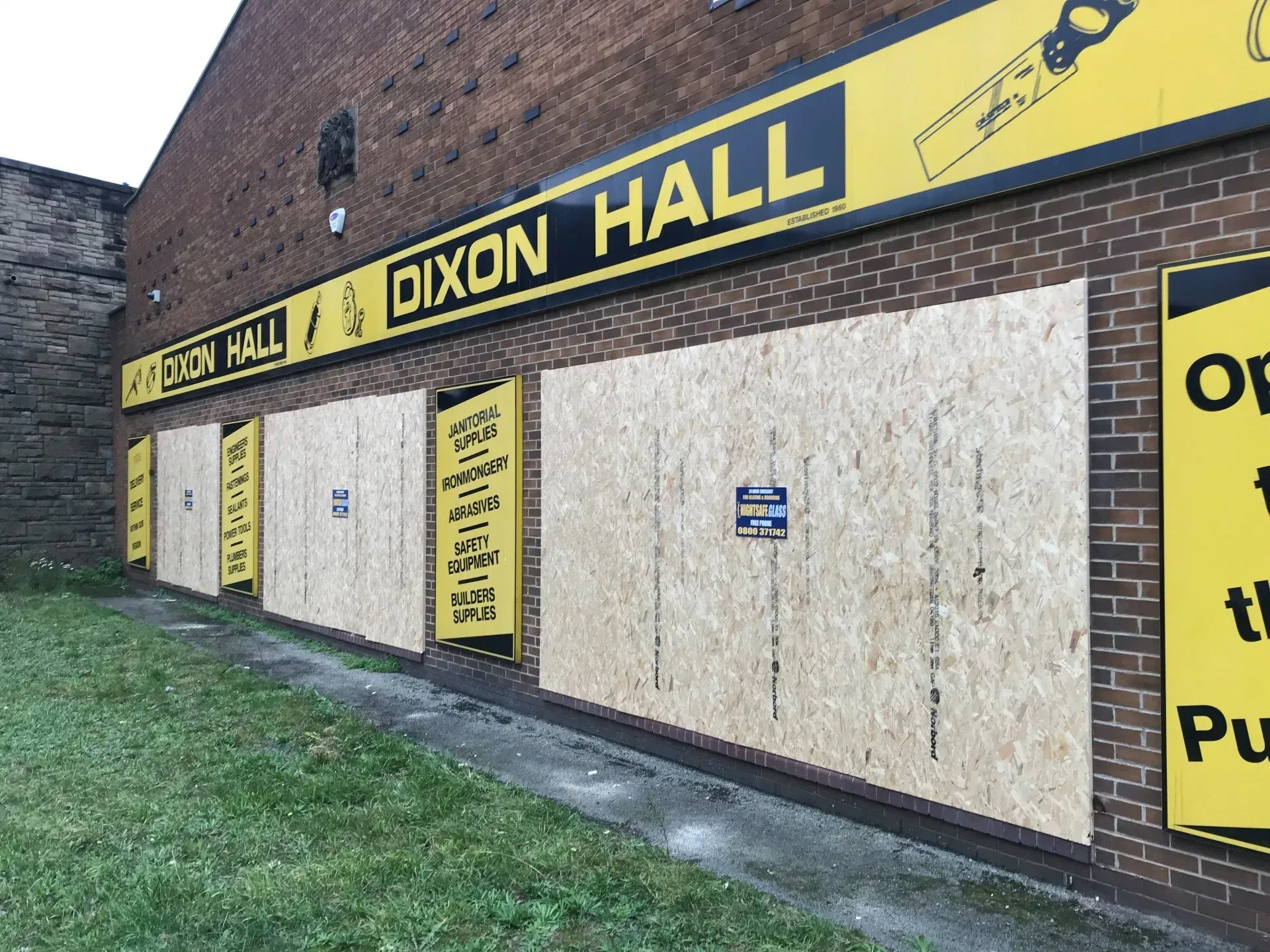 Exterior of Dixon Hall with boarded-up windows and signage. Yellow and black sign with tools, brick building.