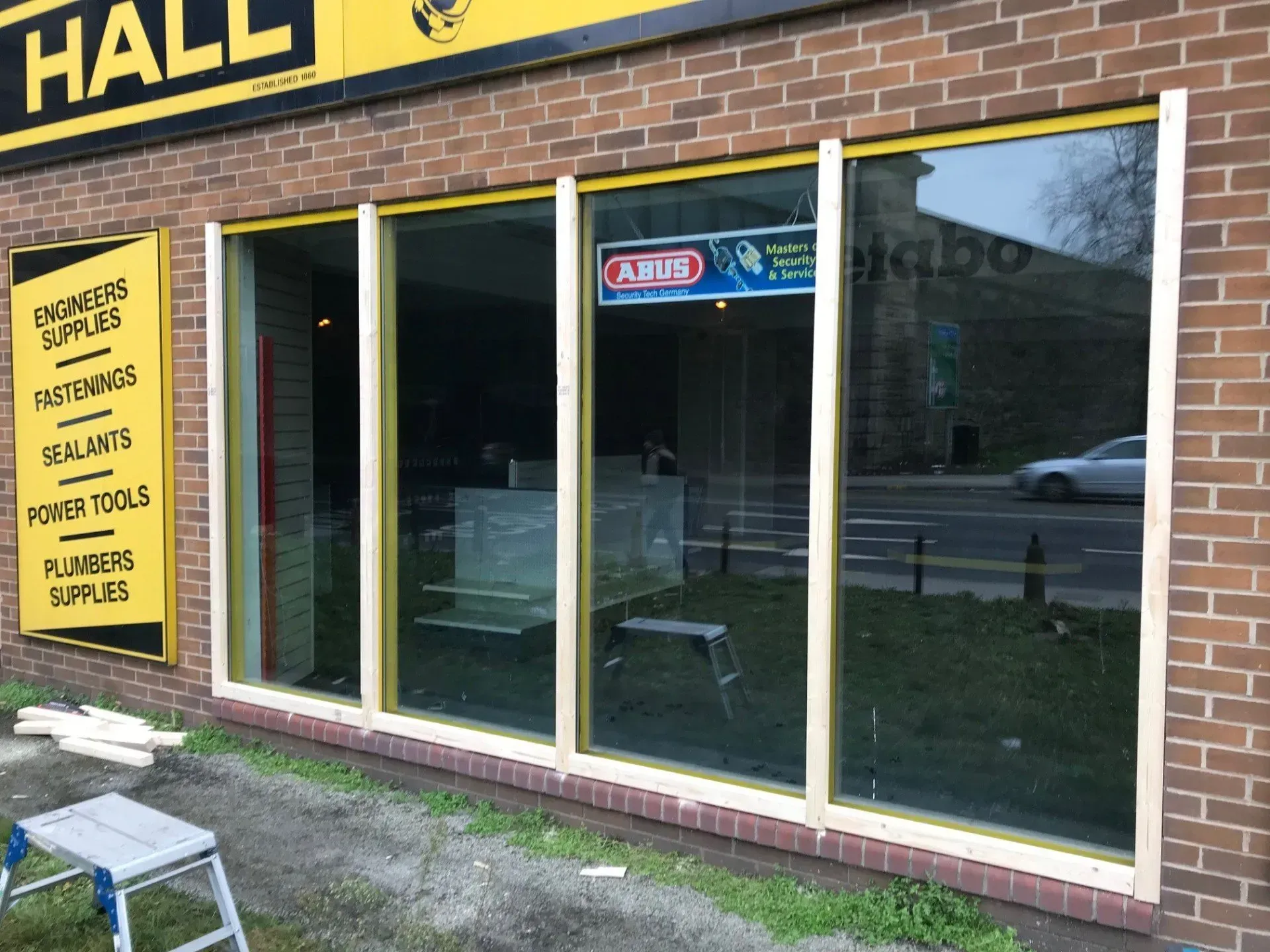 Building exterior with large windows, wooden frames, brick wall, and work tools.