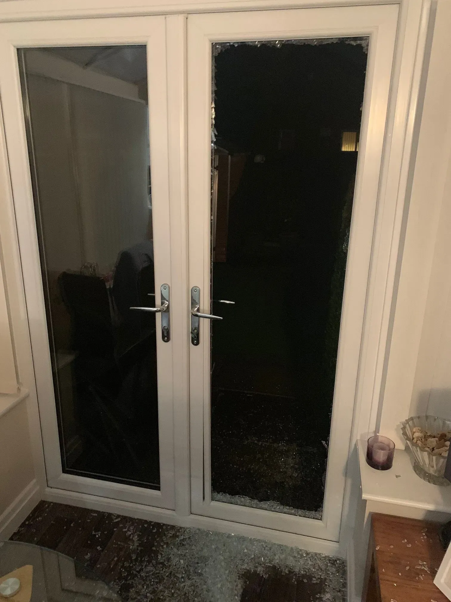 Broken glass on the bottom of a white double door. Dark backyard visible through the glass.