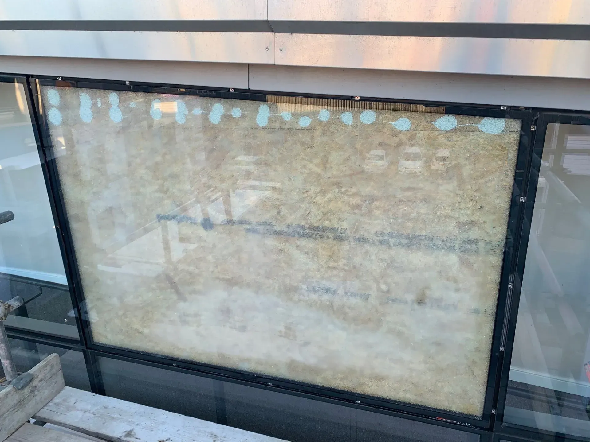 Window frame with insulation board behind glass, likely under construction.