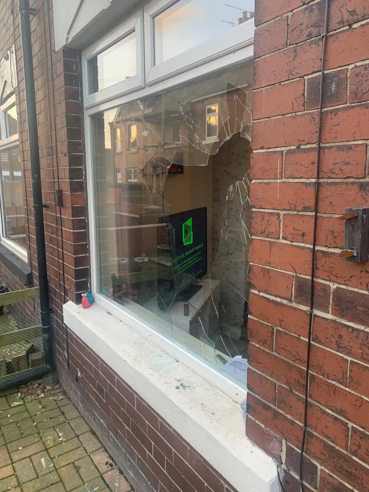 Broken window in a brick building. Shattered glass, visible interior. White window frame, red brick.
