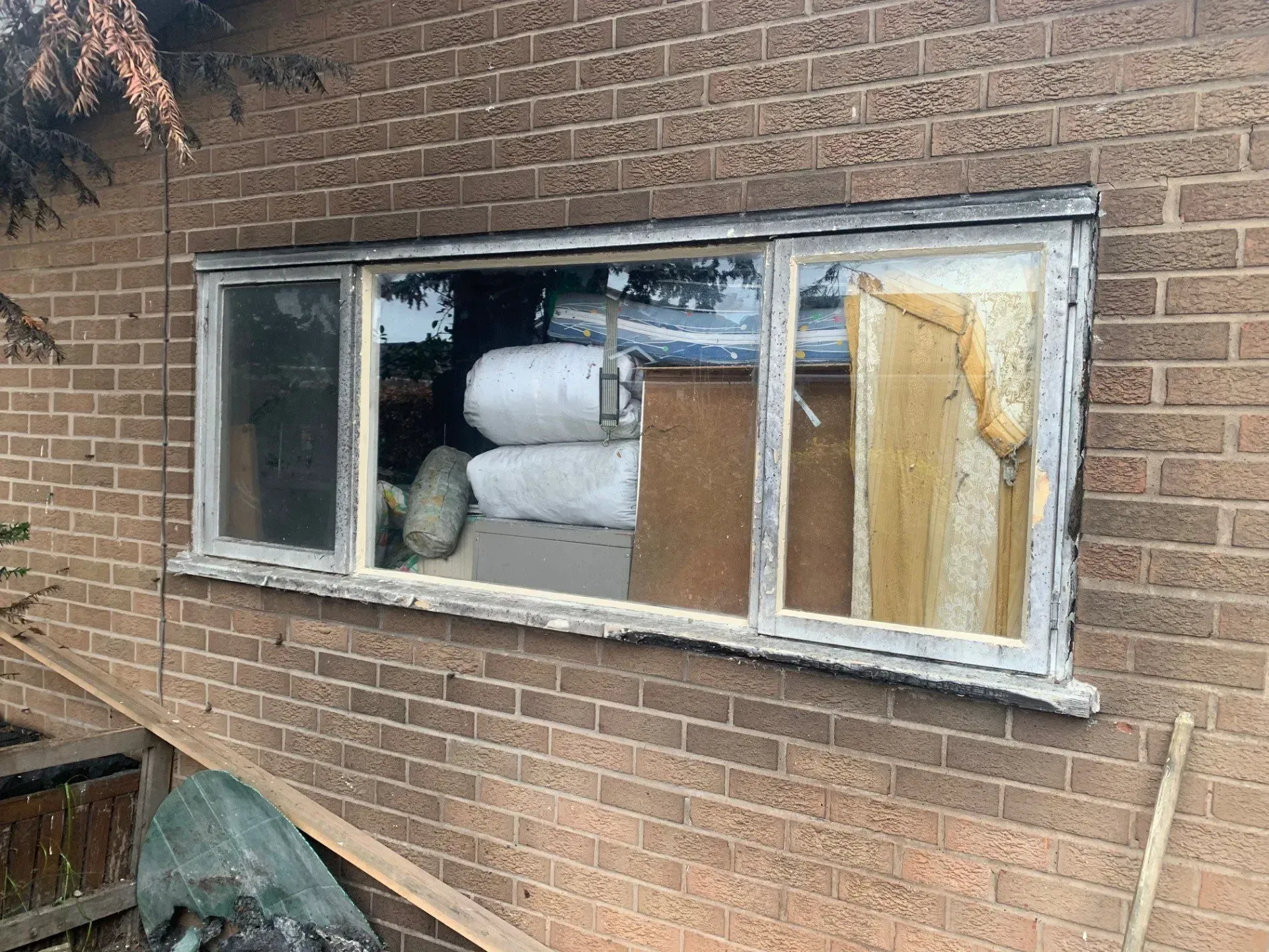 Damaged, weathered window on a brick building with visible contents inside.