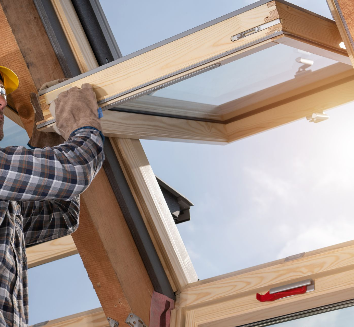 Construction worker installing a skylight window on a roof; blue sky visible.