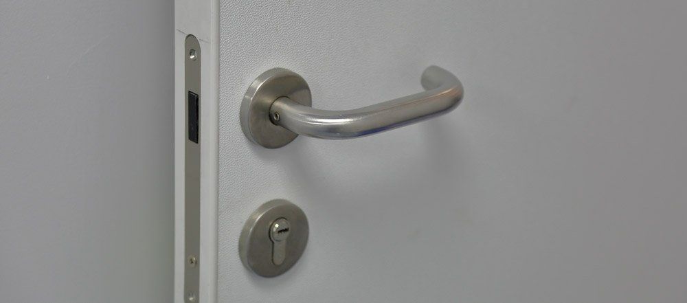 Door with a metal handle, lock, and strike plate, all silver on a white door.