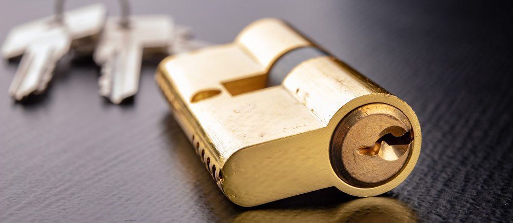 A brass door lock with a keyhole, next to a set of keys on a dark surface.