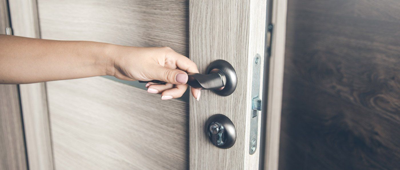 A person's hand turning a black doorknob on a light-colored wooden door.