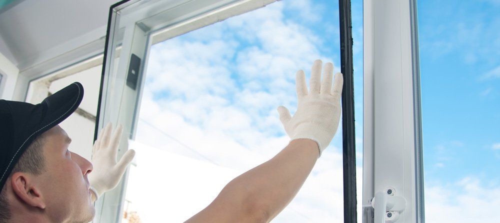 Person wearing a black cap and gloves, opening a window with a blue sky visible through it.
