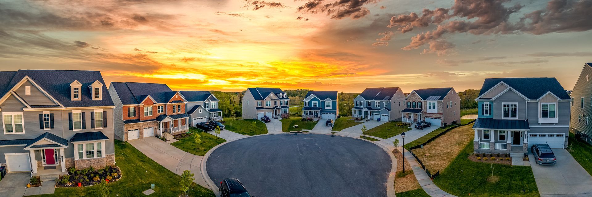 Houses in a cul-de-sac with a bright sunset sky. The houses are gray and white with dark roofs.