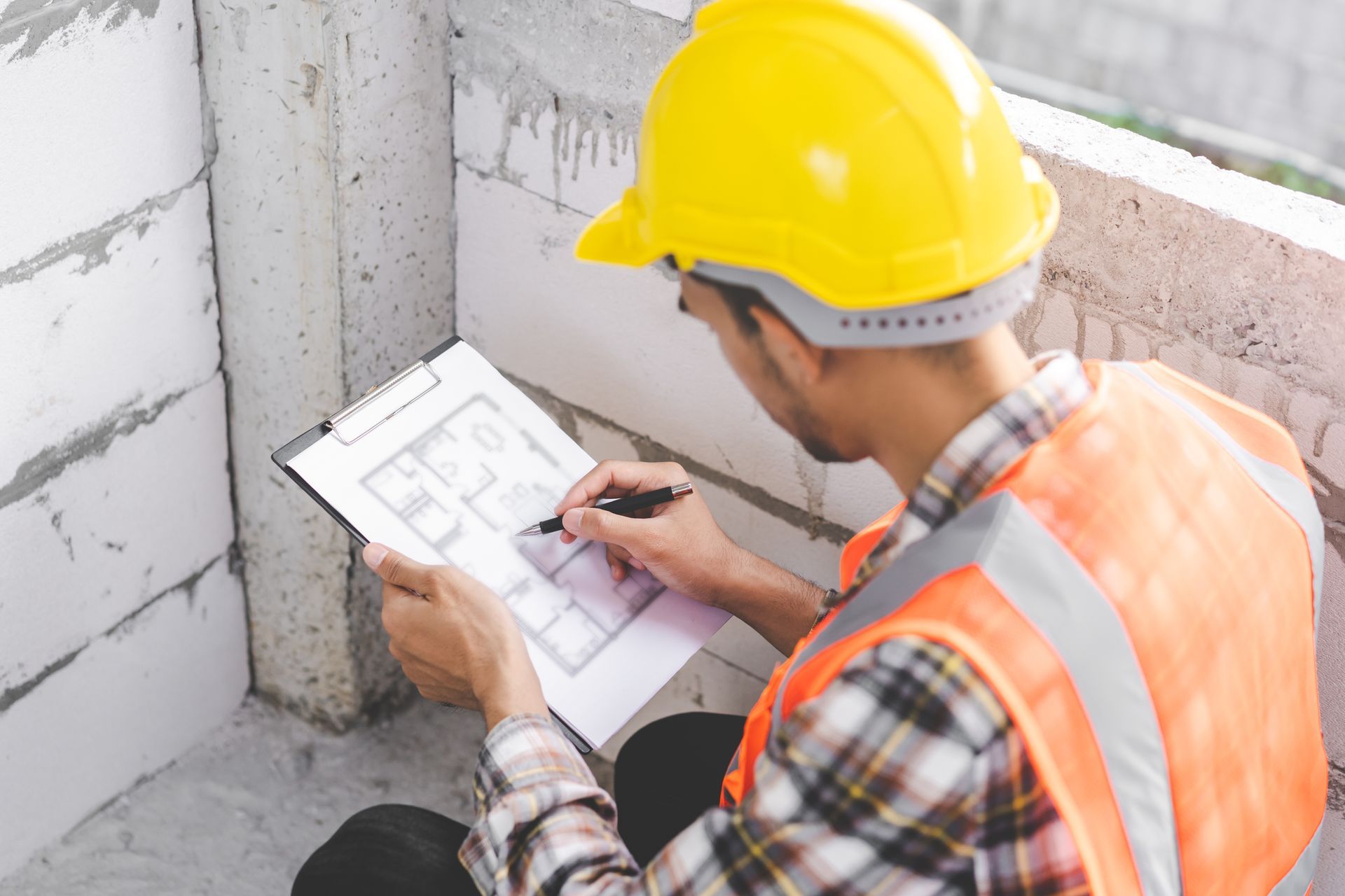 Construction worker in hard hat and vest reviews building plans at a construction site.