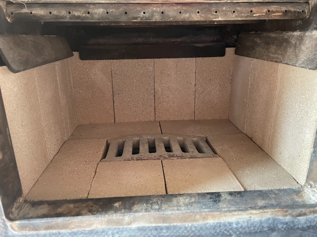 A person in black clothing cleans the interior of a tiled fireplace, using a vacuum tool with a shop vac nearby.