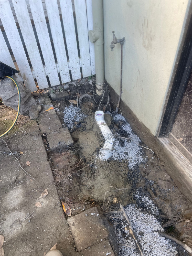 Exposed pipes near a fence and building, with a white powder spread around — Smooth Flow Plumbing Cairns in Cairns City, QLD 