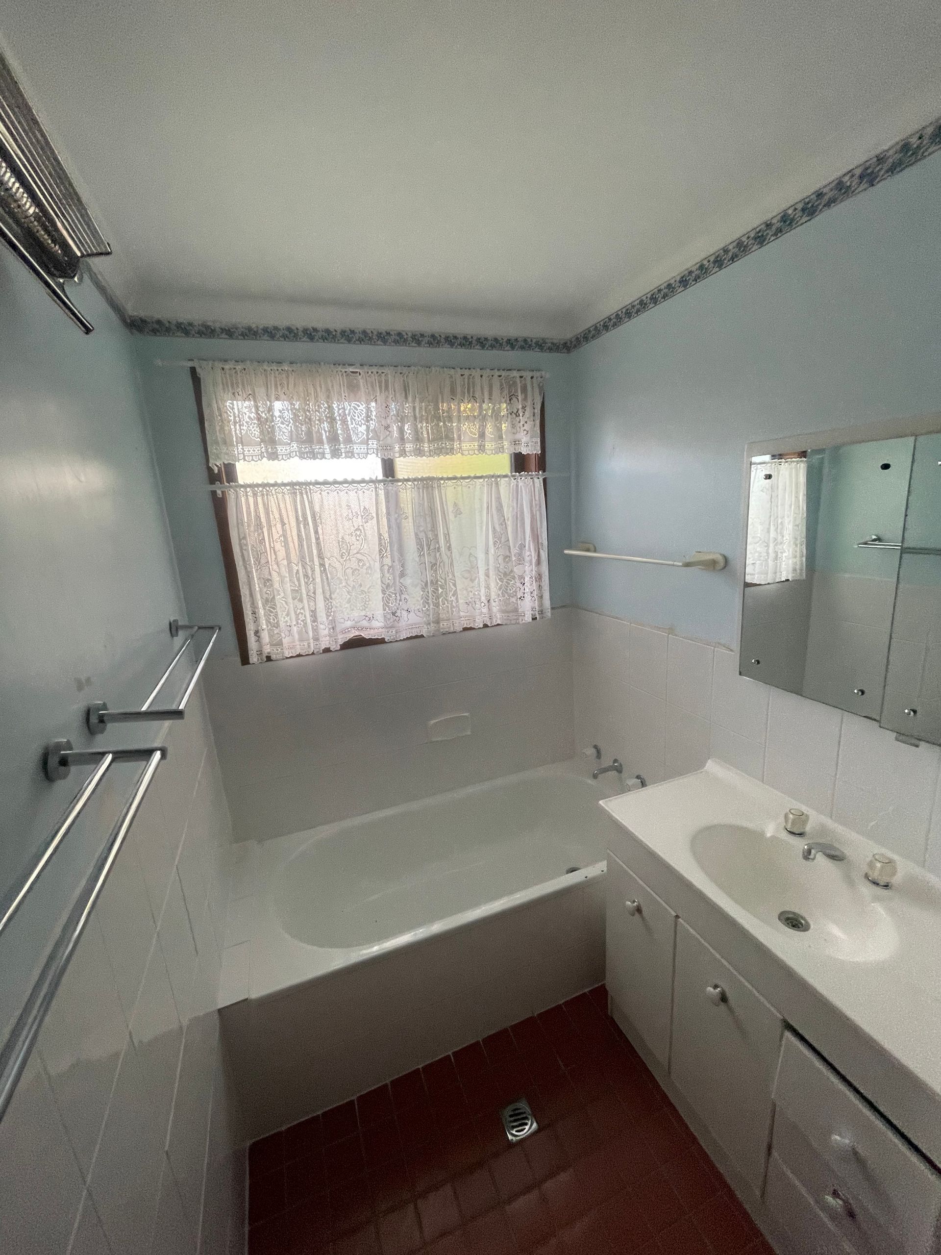 Bathroom with a bathtub, sink, mirror, and window. Blue walls with white fixtures, and a lace curtain — Smooth Flow Plumbing Cairns in Cairns City, QLD 